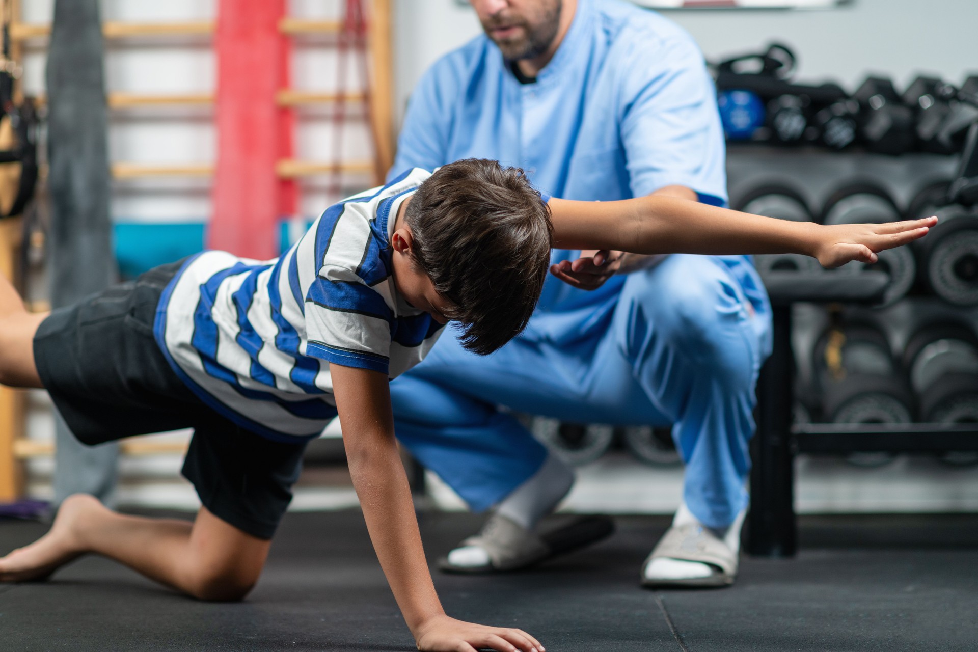 Physical therapist guiding a young boy through exercises for stability and balance, aimed at improving coordination and strength in a supportive rehabilitation session